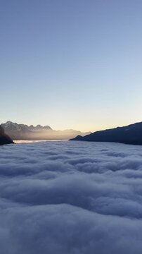 Thick clouds blanket a mountain valley at sunrise with soft light on snowy peaks