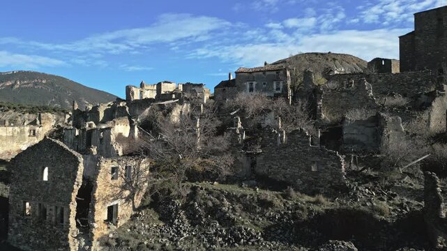 Ruined stone buildings of the historic ghost town of Esco, an abandoned village in Aragon, Spain, sitting on a hillside under a blue sky with some clouds on a sunny day