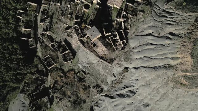 Aerial drone view flying backwards revealing the abandoned ghost town of Esco, located in the province of Zaragoza, Aragon, Spain, with its ruined stone houses and eroded landscape