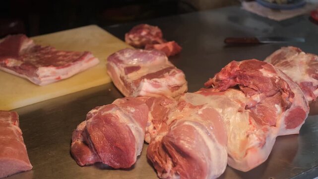 Chunks of raw pork placed on butcher counter with cutting board and preparation area at indoor market. Meat selling concept