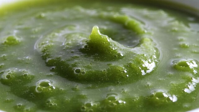 Close-up of vibrant green pureed peas with a swirl design on a white background