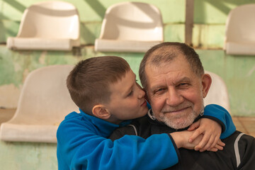 Obraz premium Young boy embracing grandfather sitting in the empty stands of a sports facility.