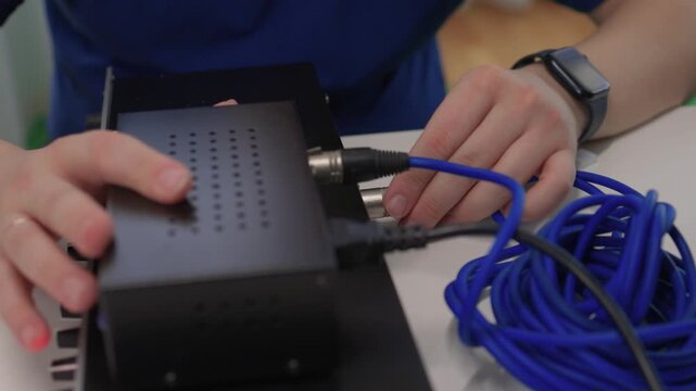 Connecting audio devices. Person meticulously plugging cable into device. Individual precisely connecting audio cables to equipment ensuring proper setup and function