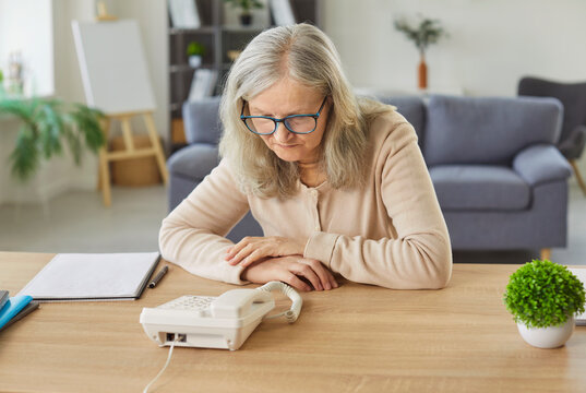Nervous senior woman waiting for phone call near telephone at home, anticipating communication and news, senior tension in a escape zone filled with anxious expectation and concern.
