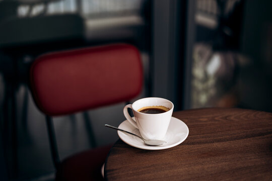 Cup of black coffee on wooden cafe table with empty seat