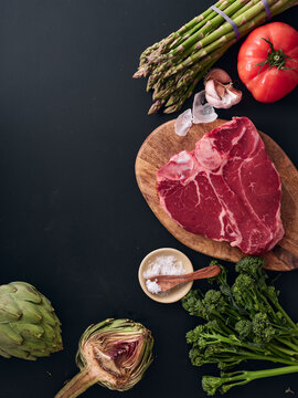 Raw t-bone steak with vegetables on black background