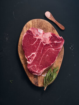 Raw t-bone steak on wooden board with herbs and salt