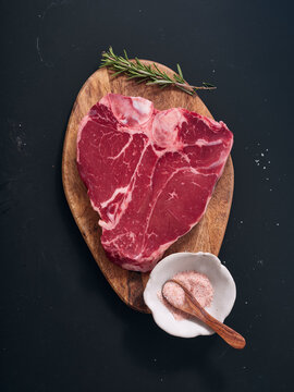 Raw t-bone steak on wooden board with herbs and seasoning