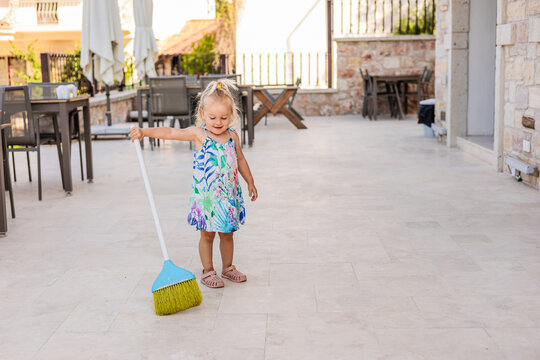 Young girl sweeping patio terrace with large broom outdoors