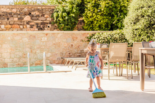 Young girl sweeping pool terrace in sunny backyard patio