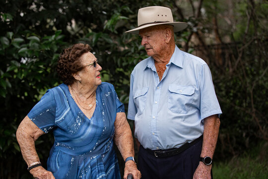 Elderly woman in blue patterned dress and rollator, talking to elderly man in light blue shirt