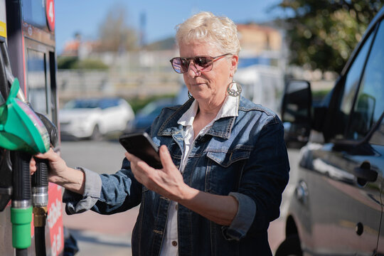 Senior woman refueling car checking phone