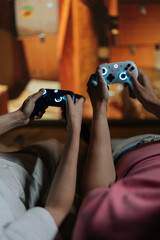 Couple holding glowing wireless controllers, immersed in virtual reality gaming on large screen at home, sharing high-tech entertainment, connection, and relaxed leisure together. © dikushin