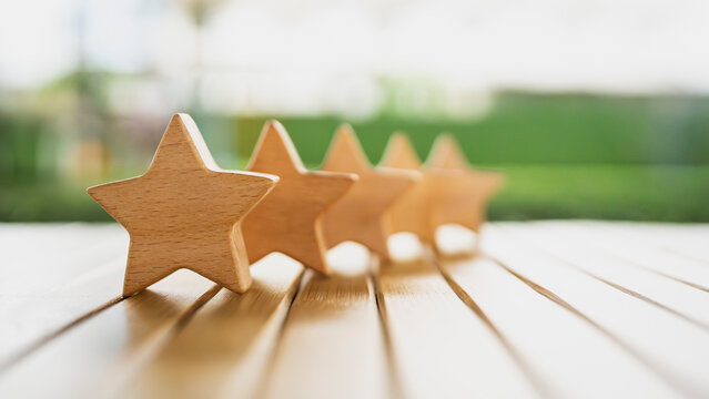 Five wooden stars arranged in a row on a wooden table with blurred green background. Concept of excellent customer feedback, top quality rating, premium service, and business success.
