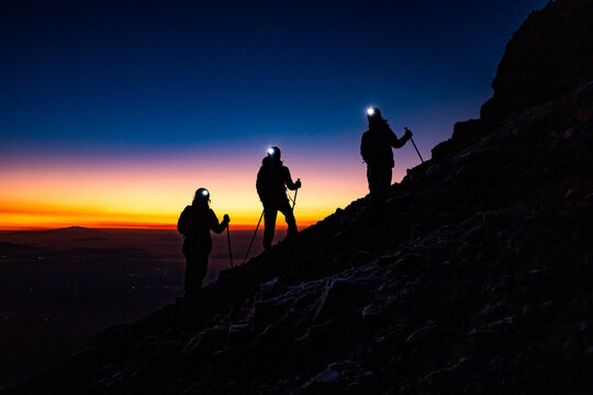 Hikers ascending mountain ridge at sunrise with headlamp