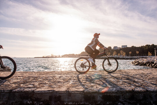 Woman riding electric bicycle along seaside at sunset