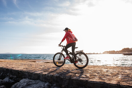 Woman riding electric bicycle on coastal promenade at sunset
