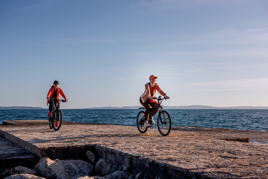 Two women friends riding e-bikes on a seaside pier at dawn