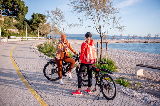 Two women friends with electric bicycles by the seaside