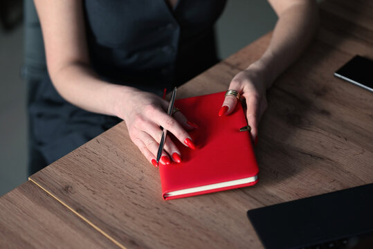 Woman writing in red notebook at office desk for business