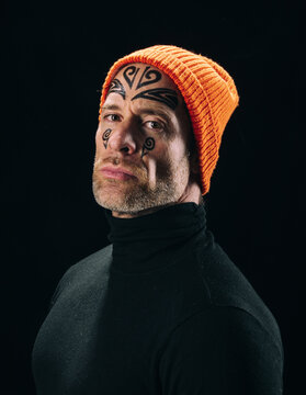 Tattooed man face portrait in orange beanie on black