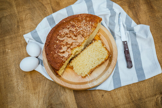 Overhead view of sponge cake on wooden board with eggs and knife