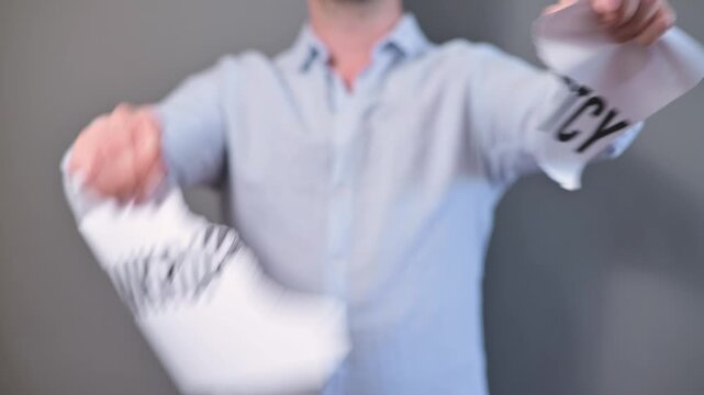 A person is seen holding a piece of paper labeled bankruptcy. The individual is actively tearing the document into pieces in a simple indoor setting