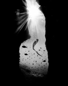 Freediver in underwater cave with sunbeams and fish