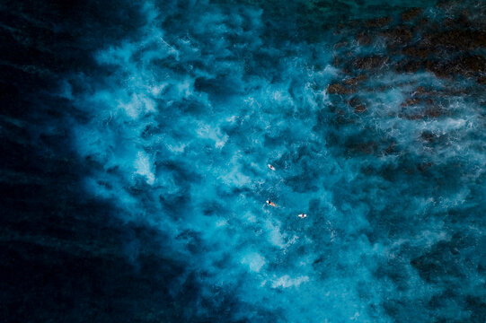 Aerial view of turquoise ocean waves with surfers below