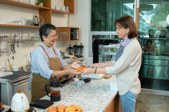 Senior cafe owner small business woman services bakery fresh croissant to customer in coffee shop, checking receipts and managing sales record showing responsibility and active aging working lifestyle