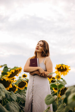Woman holding Holy Bible in sunflower field at sunset