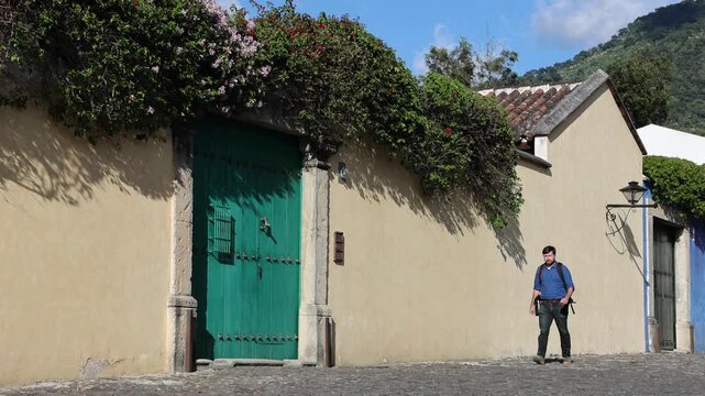 backpacker walking down scenic colonial street in antigua guatemala (backpacking latin america with large backpack) book bag back pack spanich architecture scenic tropical city