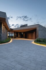Naklejka premium Modern building design features smooth lines and natural materials at dusk in a serene outdoor setting surrounded by grass and stones