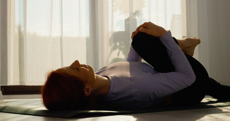 Woman practices stretching and pilates exercises on a mat in her bright living room, embracing a healthy lifestyle. Enjoy a serene morning routine filled with movement. © Binzari