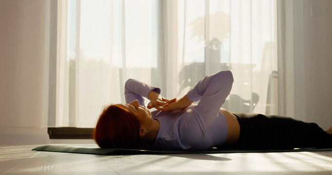 In a bright living room, a woman engages in stretching and pilates exercises on a mat. The sunny space promotes a healthy morning routine filled with movement.