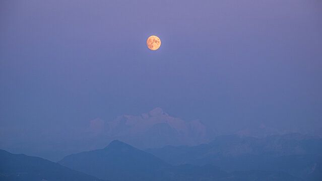 Full moon illuminating a serene blue mountain landscape