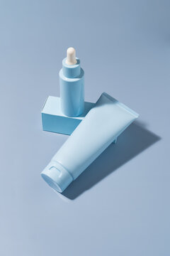 Minimal cosmetic serum bottle and cream tube on blue