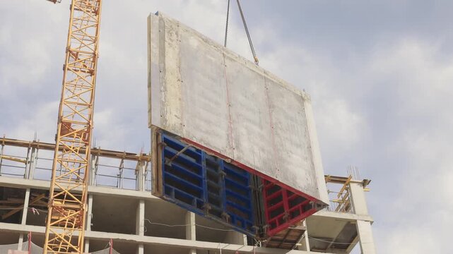 Crane lifting massive concrete panel above urban skyscrapers during construction. Cranes and rigging coordinate to install large concrete slabs in city high rises