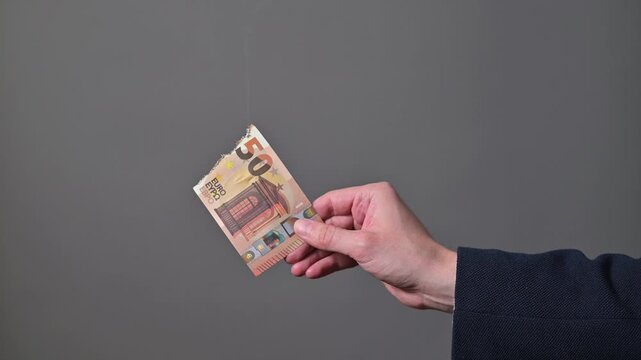 Close-up of hand holding burnt smoking euro banknote