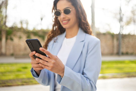 Smiling businesswoman using smartphone outdoors in blazer