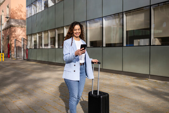 Business traveler using smartphone while pulling suitcase outdoors