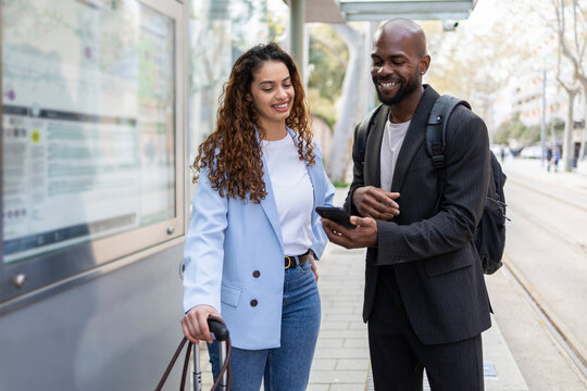 Business couple checking phone at transit stop during trip