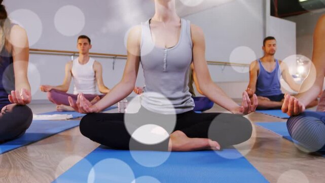 Woman lifting chest, centering on blue yoga mat as camera pulling back, bokeh drifting across faces