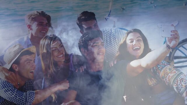 Right person raising phone, group leaning, laughing on shore, haze crossing faces for marketing
