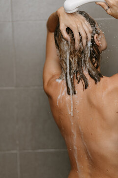 Woman rinsing shampoo from hair under shower, rear view