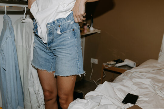 Woman getting dressed in denim shorts at home bedroom