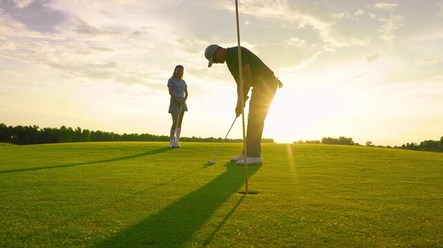 Asian man and woman golfers swing clubs together on scenic golf course. 