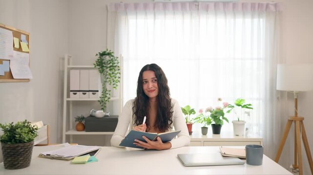 Young Hispanic woman writing while sitting at table in living room at home. 