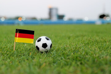 German flag standing on football field next to black and white soccer ball with soft bokeh stadium background and copy space, symbolizing international tournament energy, unity and sporting identity. © The Dell Shot by SJ