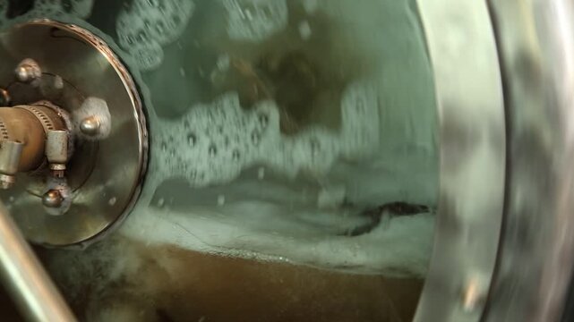 Inside view of fermentation vessel showing brewing process. Industrial brewery environment capturing fermentation process with yeast activity and equipment details